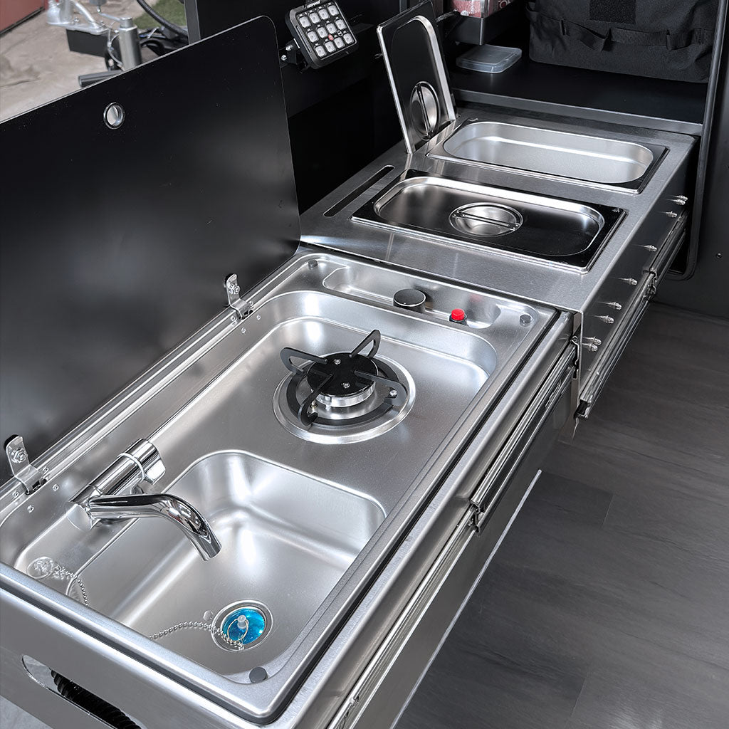 Compact Stainless steel foldable kitchen setup with sink, stove, and storage compartments in a trailer drawer.
